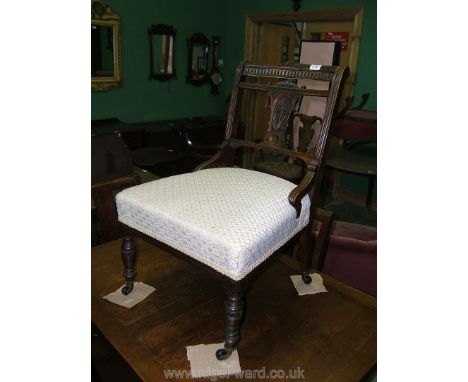 An Edwardian Walnut framed Nursing Chair having delicate carved top rail and splat, with reeded back supports, applied cream 