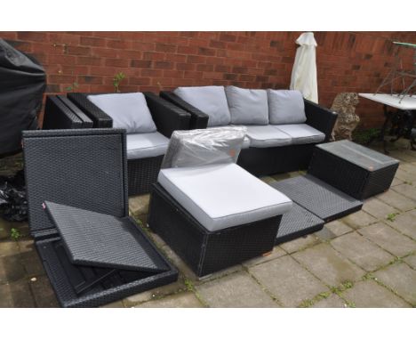 A BLACK RATTAN EFFECT GARDEN SET including a three seat sofa width 180cm a chair and stool all with cushions, a glass topped 