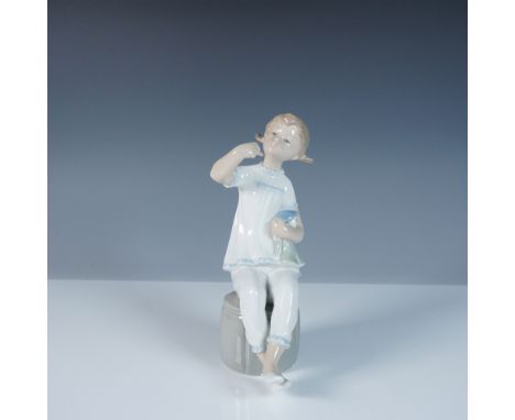 This Lladro figurine, titled Girl with Dog (#1001083), captures a touching moment of a young girl seated on a stool, gently h