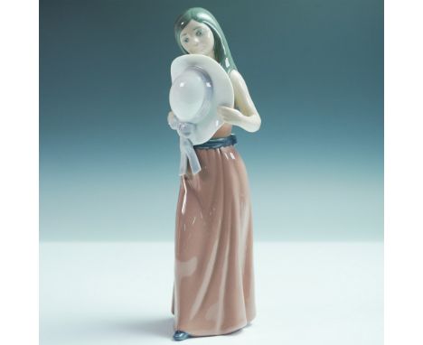 This glazed figurine depicts a shy young woman in a flowing brown dress with a blue sash, delicately holding a wide-brimmed h