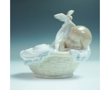 Porcelain figurine depicting a sleeping baby cradled in a woven basket with a flowing blanket held by a delicate bird. This g