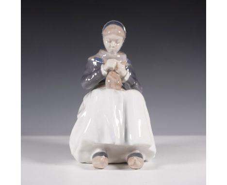 A delicate Royal Copenhagen porcelain figurine of a seated woman intently knitting. Rendered in soft hues of blue, white, and