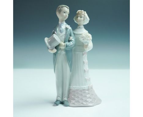 Lladro porcelain figurine depicting a bride and groom standing side by side. The groom is shown in formal attire holding a to