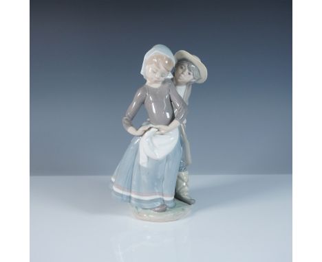 This Lladro figurine, titled Little Couple Kissing (#1001188), depicts an endearing scene of a young boy and girl in traditio