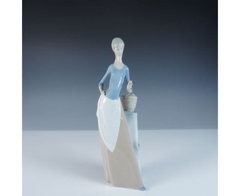 This Nao by Lladro figurine, titled Girl with Apples, features a graceful young woman leaning against a stacked pedestal with