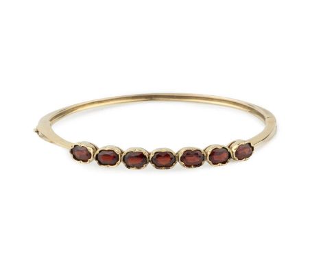 A 9ct gold and garnet hinged bangle, set with seven oval cut stones and having safety chain, stamped 375, 6.3cm wideGross wei