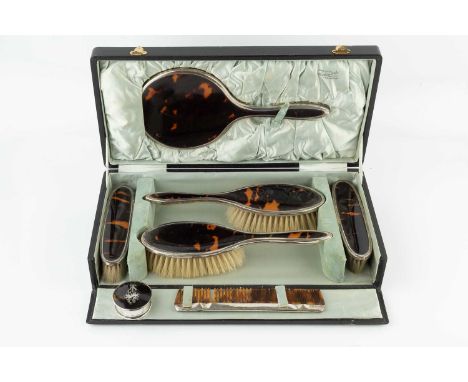 A silver mounted tortoiseshell backed dressing table set, comprising hand mirror, two hair brushes, two clothes brushes, a sm