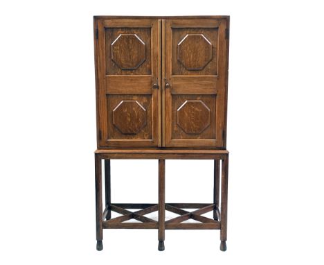 Gordon Russell (attributed), a Cotswold School Arts and Crafts oak cabinet on stand, the octagonal moulded, four panel double