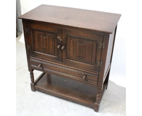 A 20th century oak linen fold panel cabinet with two cupboard doors over single drawer, supported on turned legs united by sh