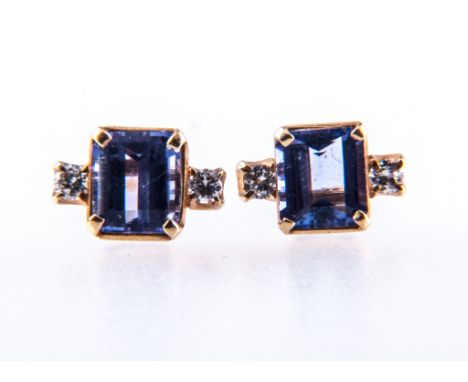 A pair of yellow metal tanzanite and diamond stud earrings, rectangular blue tanzanite, step cut stone four claw set with a b