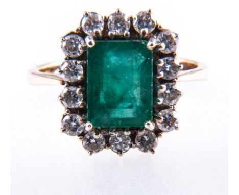 An emerald and diamond rectangular cluster ring, one step cut emerald four claw set and surrounded by fourteen brilliant cut 