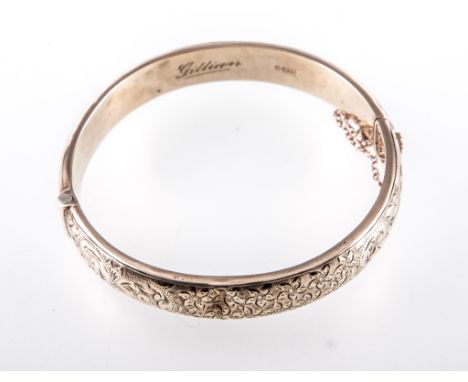 A 9 carat yellow gold half hinged bangle, 10.5mm wide hollow construction decorated with floral and leaf engraving to the fro