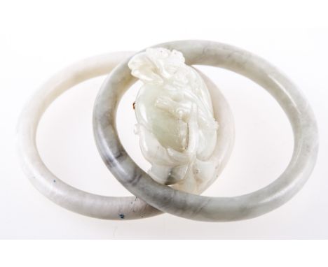 Two pale green jade bangles and a brooch, the bangles 10.5mm and 8.5mm gauge, internal diameter 65mm, the brooch depicting a 