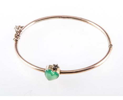 A yellow metal half hinged heart bangle, 2.6mm wide hollow tubular section with a 9mm green stone heart to the front surmount
