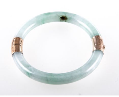 A 14 carat yellow gold and jade bangle, the half hinged 8.4mm wide pale green jade bangle having 14 carat yellow gold finely 
