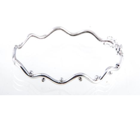 A 9 carat white gold diamond set bangle, 2.5mm wide plain polished wavy band, half hinged and set with eight diamonds to the 