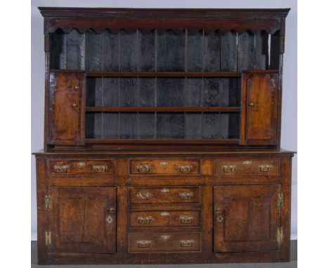 A George III oak dresser, three shelf delft rack under a moulded canopy and incorporating two end cupboard doors, the base fi