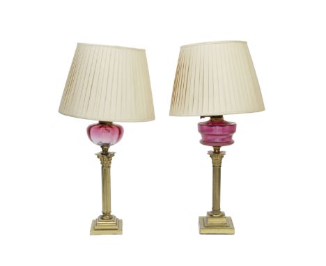 A pair of Victorian brass and ruby glass oil burnersMounted as lamps, 19th centuryWith cream silk shades, 76cm high, 29 1/2in