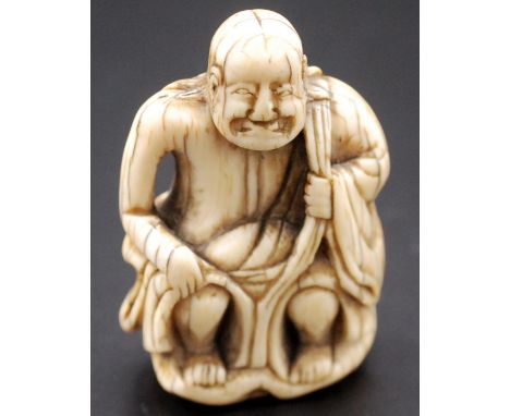 A Japanese ivory netsuke of a Rakan seated upon a holding his robes at his shoulder and knee,a gourd hanging over his left sh