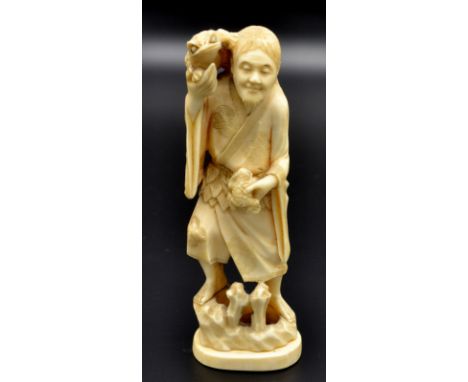 A Japanese ivory okimono of Sennin Gama in long robe with leaf sash and decorated with diaper motifs and standing upon a rock