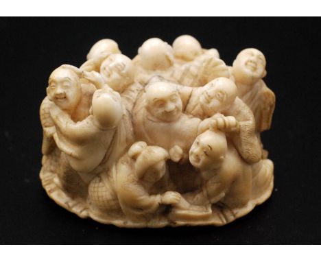 A Japanese ivory netsuke of nine smiling and laughing Hotei looking male figures clustered together, attended by a single fem