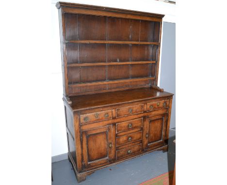 A pine dresser in George III style and possibly of the period, the upper section with open shelf, the base with drawers, pane