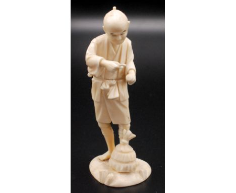 A Japanese ivory sectional ivory figure of a peasant standing holding a pipe, at his feet a straw hive like package. Late Mei