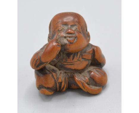 A Japanese wooden netsuke of a seated boy holding a mask behind his back and making a bekkako gesture, 19th century.