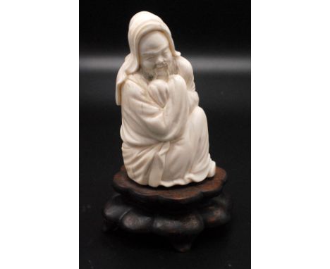 A Chinese seated figure of a bearded Lohan his arms crossed at chest high and enveloped within the folds of a hooded cloak. 1
