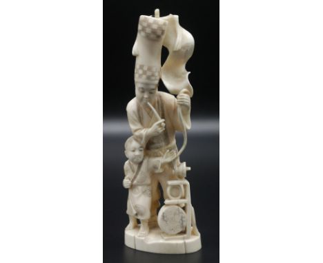 A Japanese walrus ivory figure group of a street entertainer and a youth assistant, the former shown standing smoking a pipe,