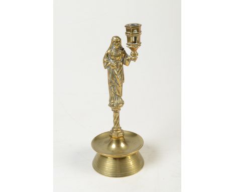 A 16th century style brass candlestick the nozzle held by a figure on short spiral stem with bell shape  base, height 21.5cm.