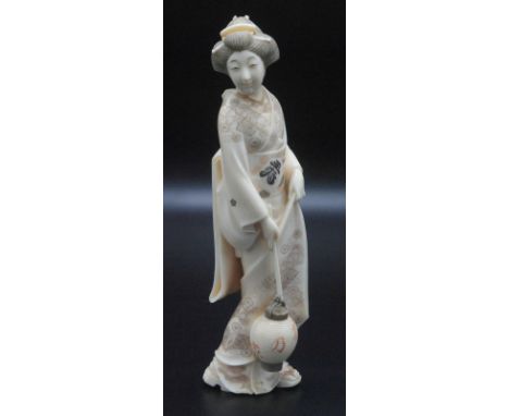 A finely carved Japanese ivory okimono, a Geisha in walking out kimono engraved with flowers and decorative fan shaped panels