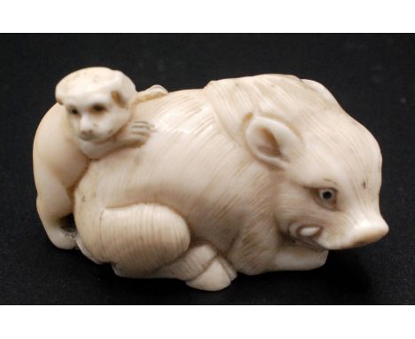 A Japanese ivory netsuke, a recumbent boar with a dog trying to climb upon its back, signed. Late 19th century. Width 5cm.