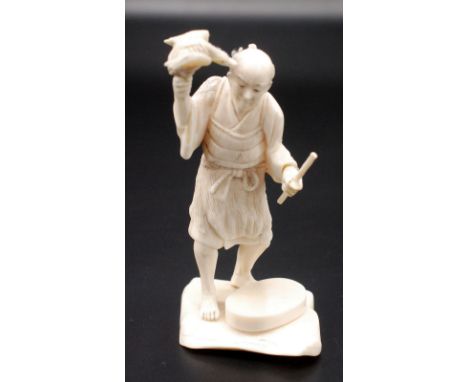 A Japanese ivory okimono, a standing cormorant fisherman holding a cormorant at shoulder high in his right hand, a baton in h