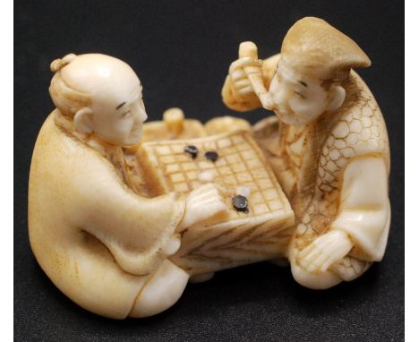 A Japanese ivory netsuke, two gentlemen seated at a game board playing "Go", one smoking and wearing a Jurojin style hat, sig