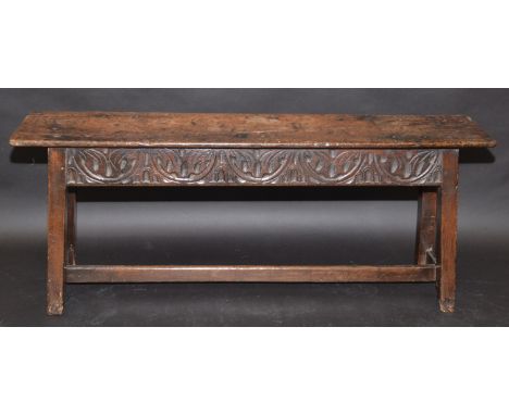 A 17th century oak joined bench, the top a single plank on a frieze carved to each side, the square section legs with low "H"