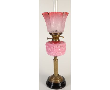 A Victorian oil lamp with a pink glass fount on a brass column and with an etched cranberry glass shade.