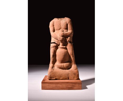 Ca. AD 100.A fine Roman hollow red terracotta statuette depicting an infant child portrayed squatting over a storage vessel. 