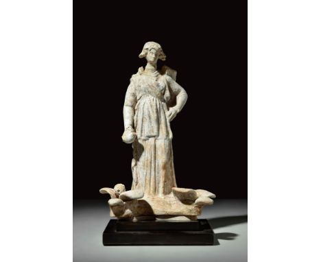 Ca. 300 BC.A pottery figure depicting a woman standing in contrapposto and wearing a tightly-wrapped himation over a long chi