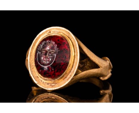 Ca. AD 100 - 300.A Roman garnet intaglio depicting a head of Putto. The intaglio is set in a high carat (21 ct), possibly lat