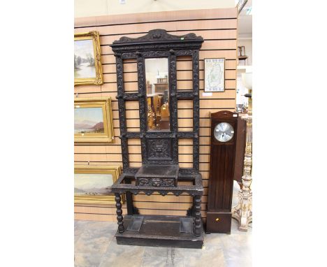 A late Victorian oak ebonised hall stand, with a mirror back, the whole machine carved in low relief, with two integral stick