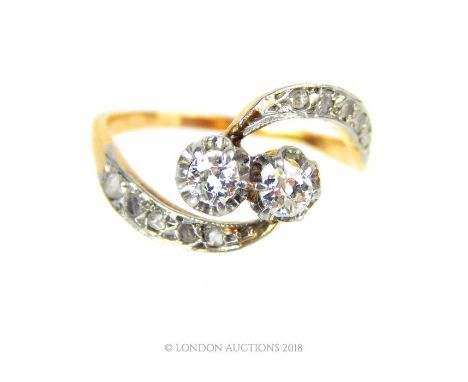 An 18 ct and platinum, French, Art Nouveau, two diamond, cross over ring, with swirling shoulders each set with five, old cut