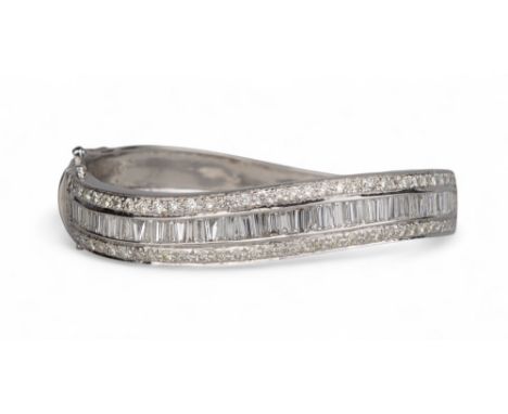 Contemporary A heavy diamond set bangle. The top wavy band centrally set with baguette diamonds, flanked by a row of brillian
