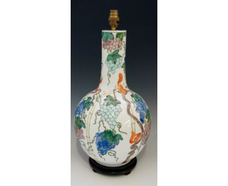 A porcelain lamp of baluster shape with tall neck, decorated overall with vine leaves and grapes, hardwood base, mounted for 