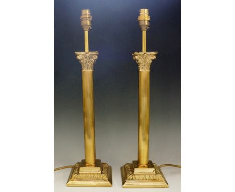 A brass Corinthian column standard lamp, 138cm high; together with two matching table lamps and unused silk shades for each (