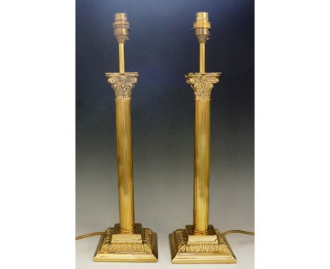 A brass Corinthian column standard lamp, 138cm high; together with two matching table lamps and unused silk shades for each (