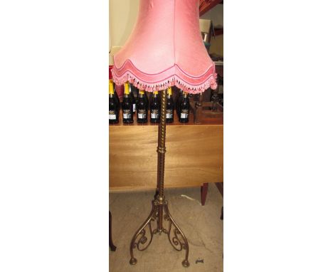 A brass standard lamp with a twisting column on three legs with floral scrolling panels