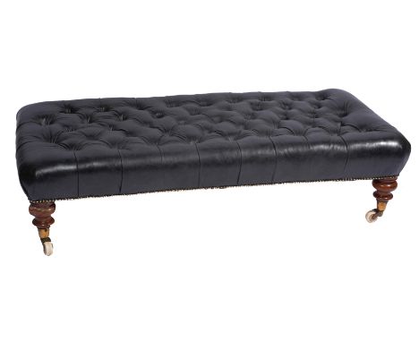 A LEATHER BUTTON UPHOLSTERED LOW STOOL standing on turned tapering legs, terminating in brass feet on ceramic castors stamped