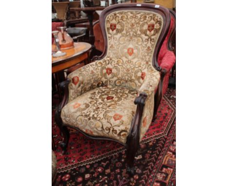 A VICTORIAN MAHOGANY FRAMED LIBRARY ARMCHAIR with overstuffed upholstered serpentine fronted seat and standing on carved scro