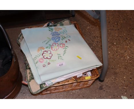 A wicker basket and contents of various vintage table cloths, cushion overs etc. 